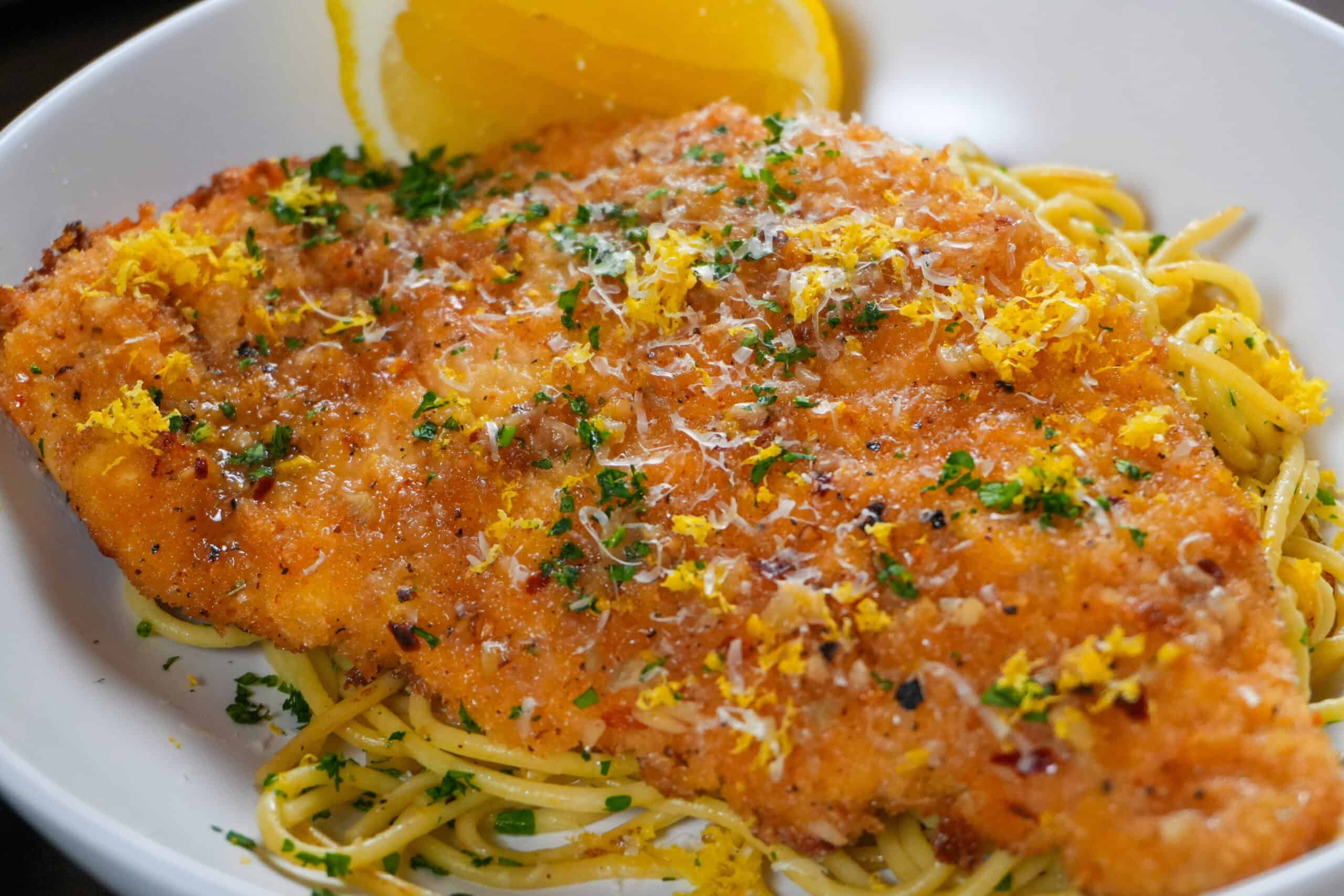 Crispy breaded chicken cutlet with spaghetti, herbs, and lemon garnish for a gourmet poultry dish.